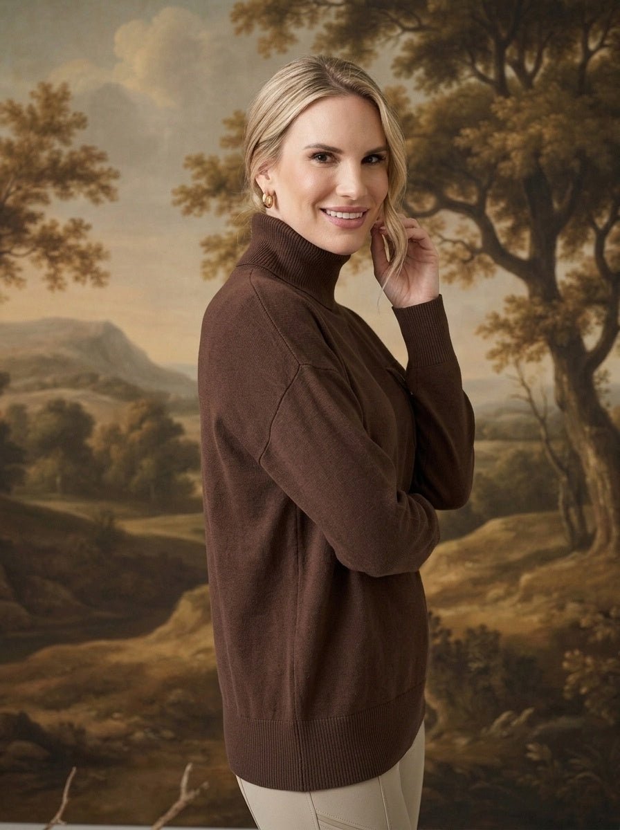 A woman wearing a brown graced Remy turtleneck sweater with a chest pocket, posing against a landscape backdrop.