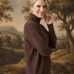 A woman wearing a brown graced Remy turtleneck sweater with a chest pocket, posing against a landscape backdrop.