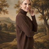 A woman wearing a brown graced Remy turtleneck sweater with a chest pocket, posing against a landscape backdrop.