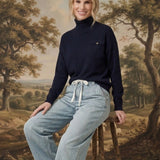 graced Remy turtleneck sweater in navy with a chest pocket, worn by a woman sitting on a wooden stool