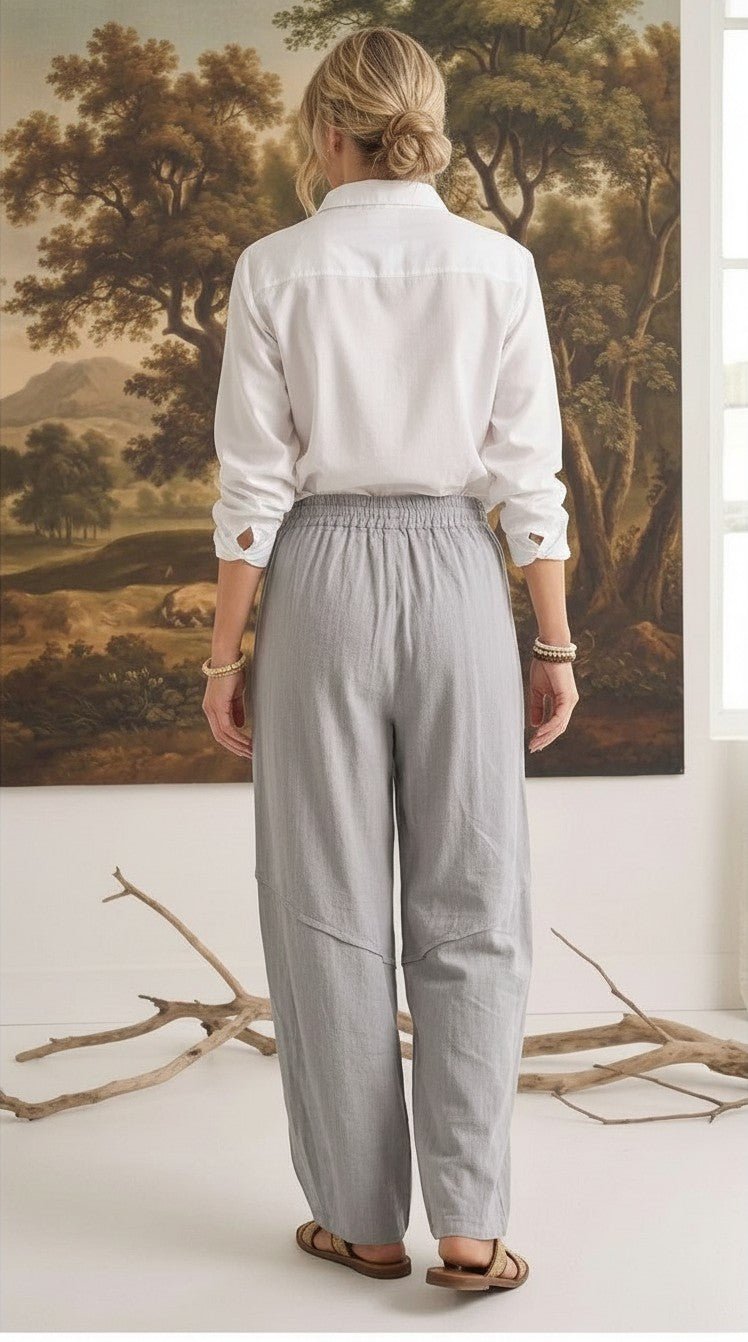 Back view of a woman wearing graced relaxed grey striped pants and a white shirt in a studio setting