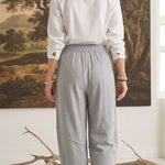 Back view of a woman wearing graced relaxed grey striped pants and a white shirt in a studio setting