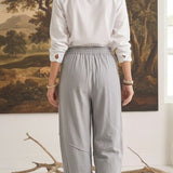 Back view of a woman wearing graced relaxed grey striped pants and a white shirt in a studio setting