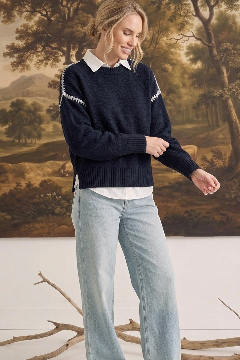 graced The Sheila Sweater in navy blue with white shoulder stitching, worn over a white shirt and light wash jeans