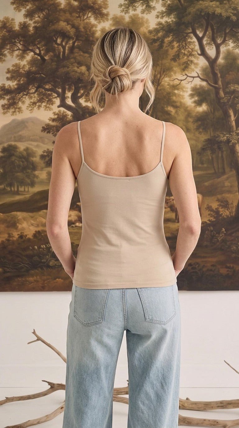 Back view of a woman wearing a light taupe graced fitted cami with spaghetti straps paired with light wash jeans.