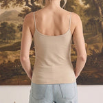 Back view of a woman wearing a light taupe graced fitted cami with spaghetti straps paired with light wash jeans.