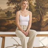 graced model wearing a white fitted spaghetti strap cami with beige jeans, sitting on a wooden bench