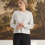 A woman wearing a graced Susie diamond pointelle floral sweater in light grey with delicate knit patterns.