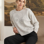 graced Susie sweater in cream with diamond pointelle and floral pattern worn by a woman sitting on a chair
