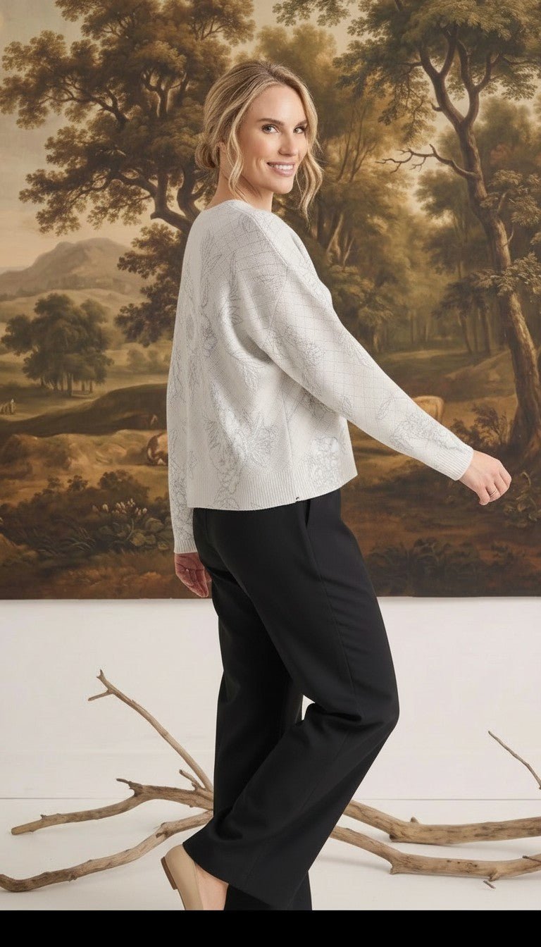 A woman wearing a graced Susie diamond pointelle floral sweater in white, paired with black trousers, side view.