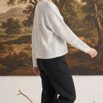 A woman wearing a graced Susie diamond pointelle floral sweater in white, paired with black trousers, side view.