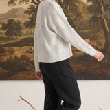 A woman wearing a graced Susie diamond pointelle floral sweater in white, paired with black trousers, side view.
