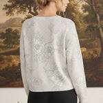 Back view of a woman wearing a graced diamond pointelle floral sweater in a light grey fine gauge knit fabric.