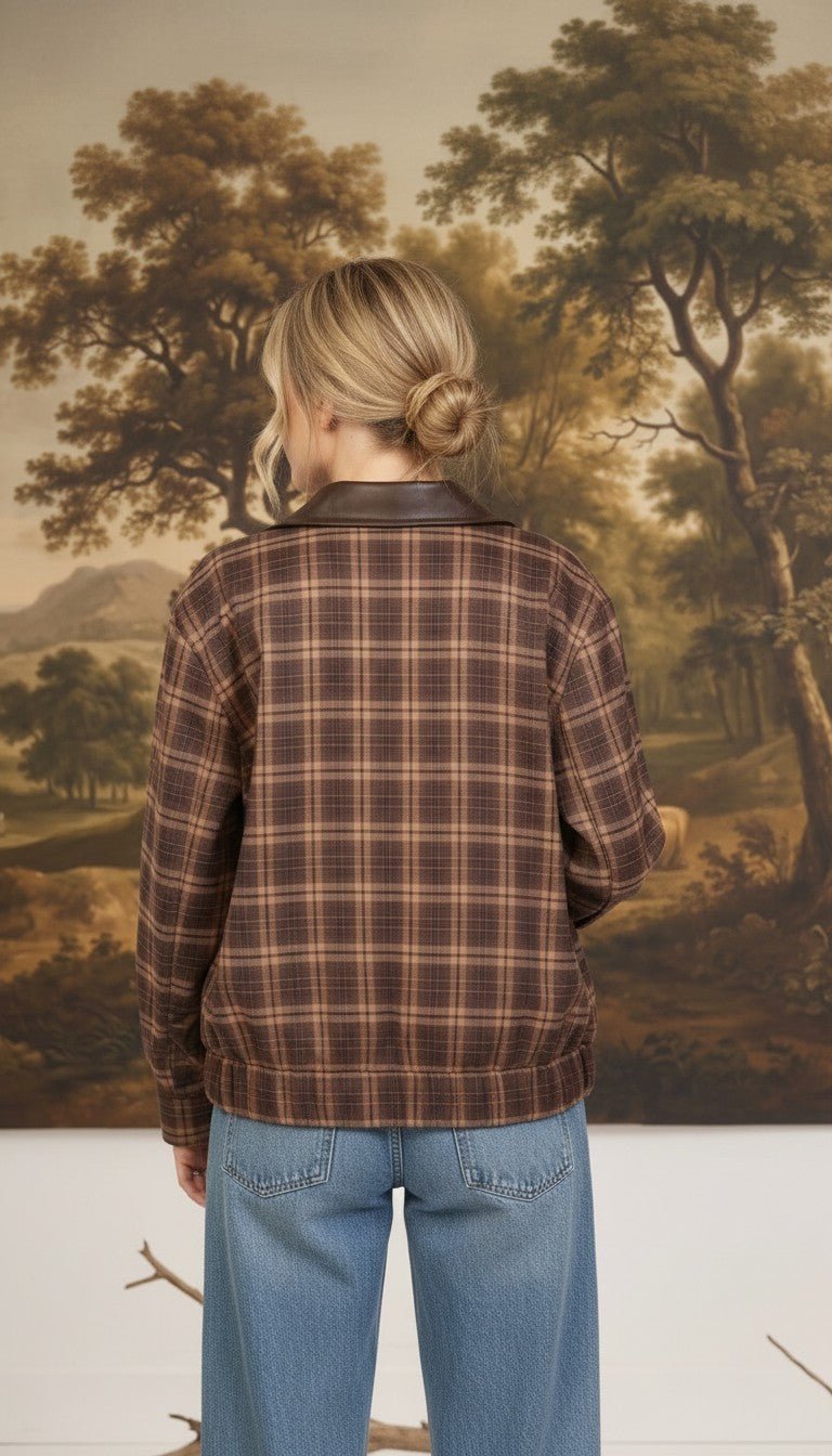 Back view of a woman wearing a graced brown plaid bomber jacket with leather collar accents and blue jeans