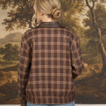 Back view of a woman wearing a graced brown plaid bomber jacket with leather collar accents and blue jeans
