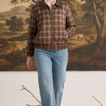 Model wearing a graced brown plaid bomber jacket with leather collar accents and a front zipper, paired with blue jeans