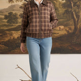 Model wearing a graced brown plaid bomber jacket with leather collar accents and a front zipper, paired with blue jeans