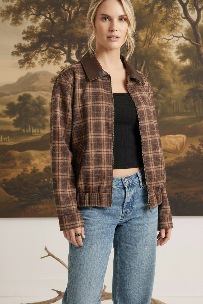 Model wearing a graced brown plaid bomber jacket with leather collar accents over a black top and blue jeans