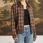 Model wearing a graced brown plaid bomber jacket with leather collar accents over a black top and blue jeans