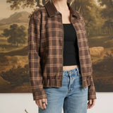 Model wearing a graced brown plaid bomber jacket with leather collar accents over a black top and blue jeans