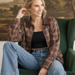 graced Tessa bomber jacket in brown plaid with leather collar, worn by a smiling woman in a green armchair