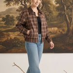 Model wearing a graced brown plaid bomber jacket with leather collar and trim, paired with blue jeans.