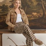 Model wearing graced Tina plaid checker pants in brown and white with a denim jacket, sitting on a wooden bench.