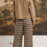 Model wearing graced Tina plaid checker pants in brown and white with a tan denim jacket, back view.