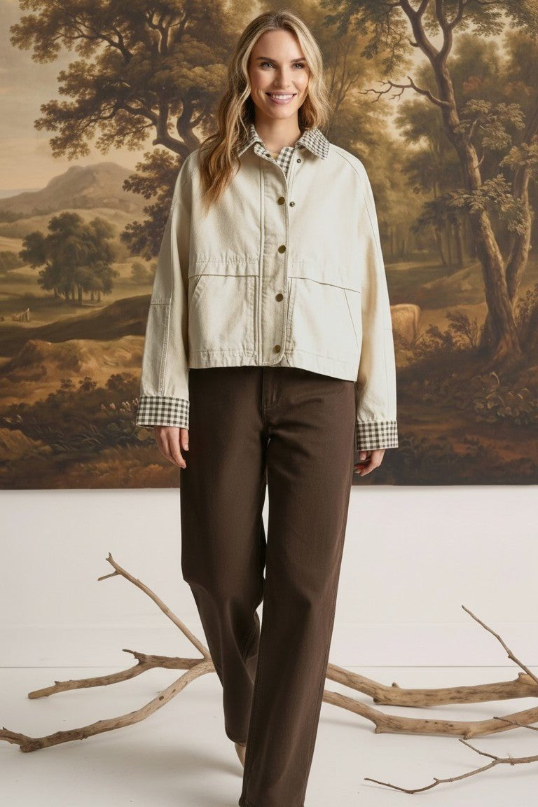 Woman wearing a graced Willow Barn Jacket in cream with a gingham collar and cuffs, paired with dark brown trousers.