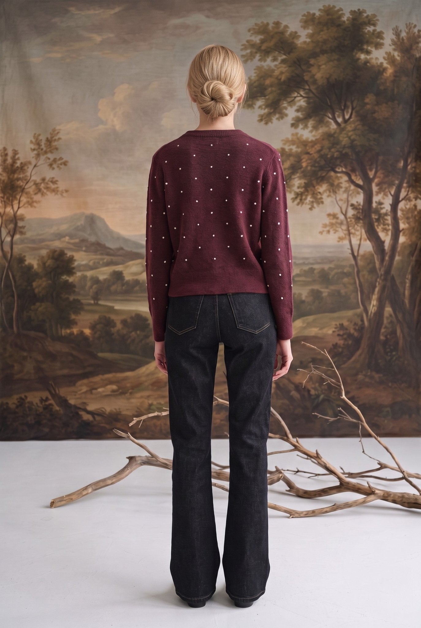 Back view of a model wearing a graced burgundy wool-blend cardigan with cream dots and dark denim jeans